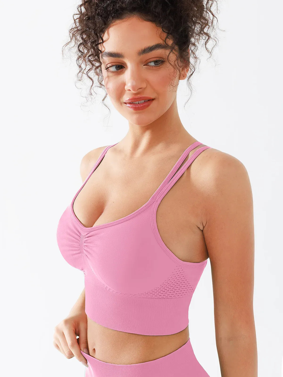 A model wearing a BRXL® B R X L™ Seamless Criss Cross Spaghetti Racerback Sports Bra Baby Pink / XS